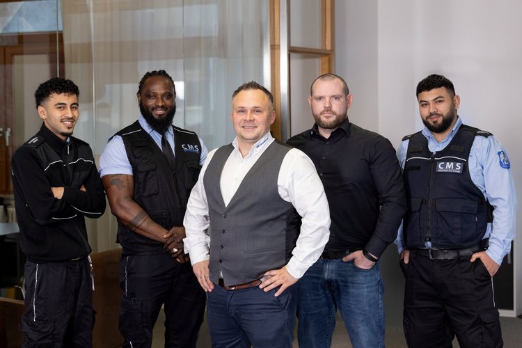 Geschäftsführer von CMS steht inmitten von vier Erwachsenen, die ihre Ausbildung bei CMS absolvieren. 