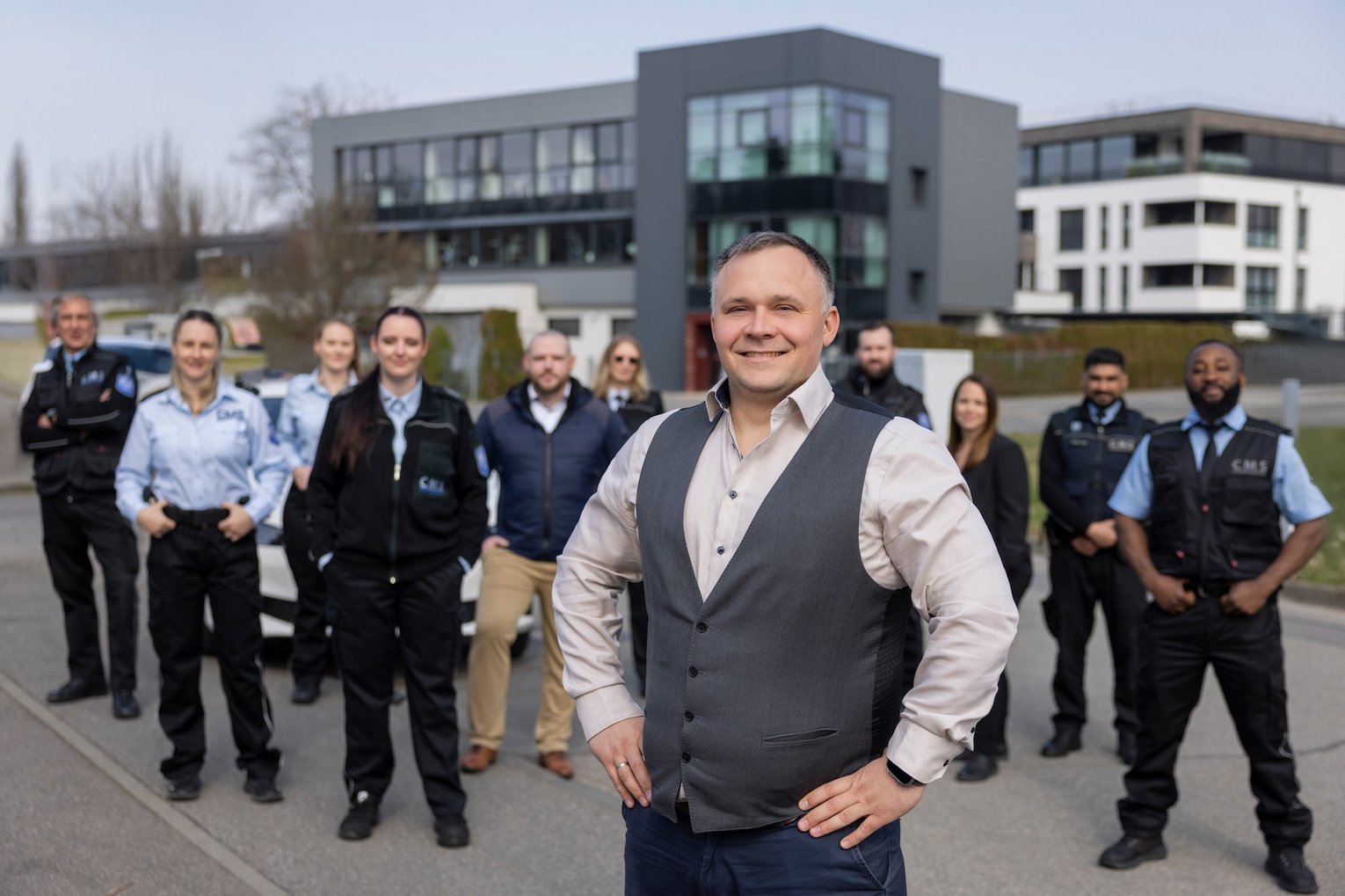 Geschäftsführer mit Team des CMS Sicherheitsdienstes steht vor modernem Bürogebäude und präsentiert das Unternehmen